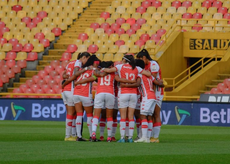 Equipe feminina de futebol reunida em círculo no campo antes de uma partida.