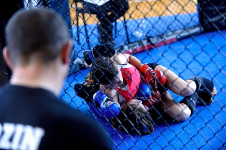 Natália Silva faz história e conquista primeiro cinturão feminino peso-mosca do Brasil no UFC Duas lutadoras treinam MMA dentro de uma jaula enquanto um treinador observa.